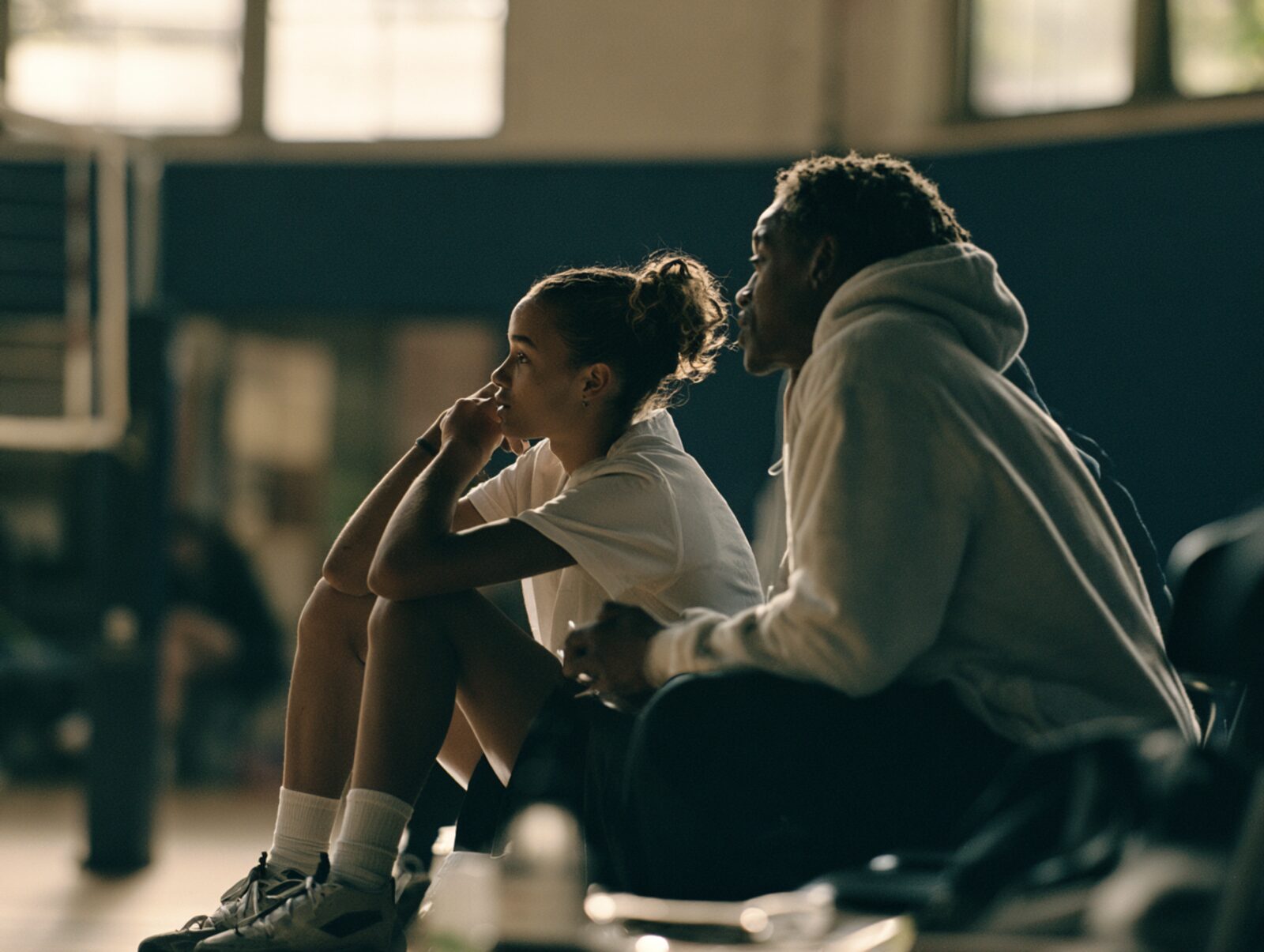 A mentor and a young athlete watching practice together from the sideline